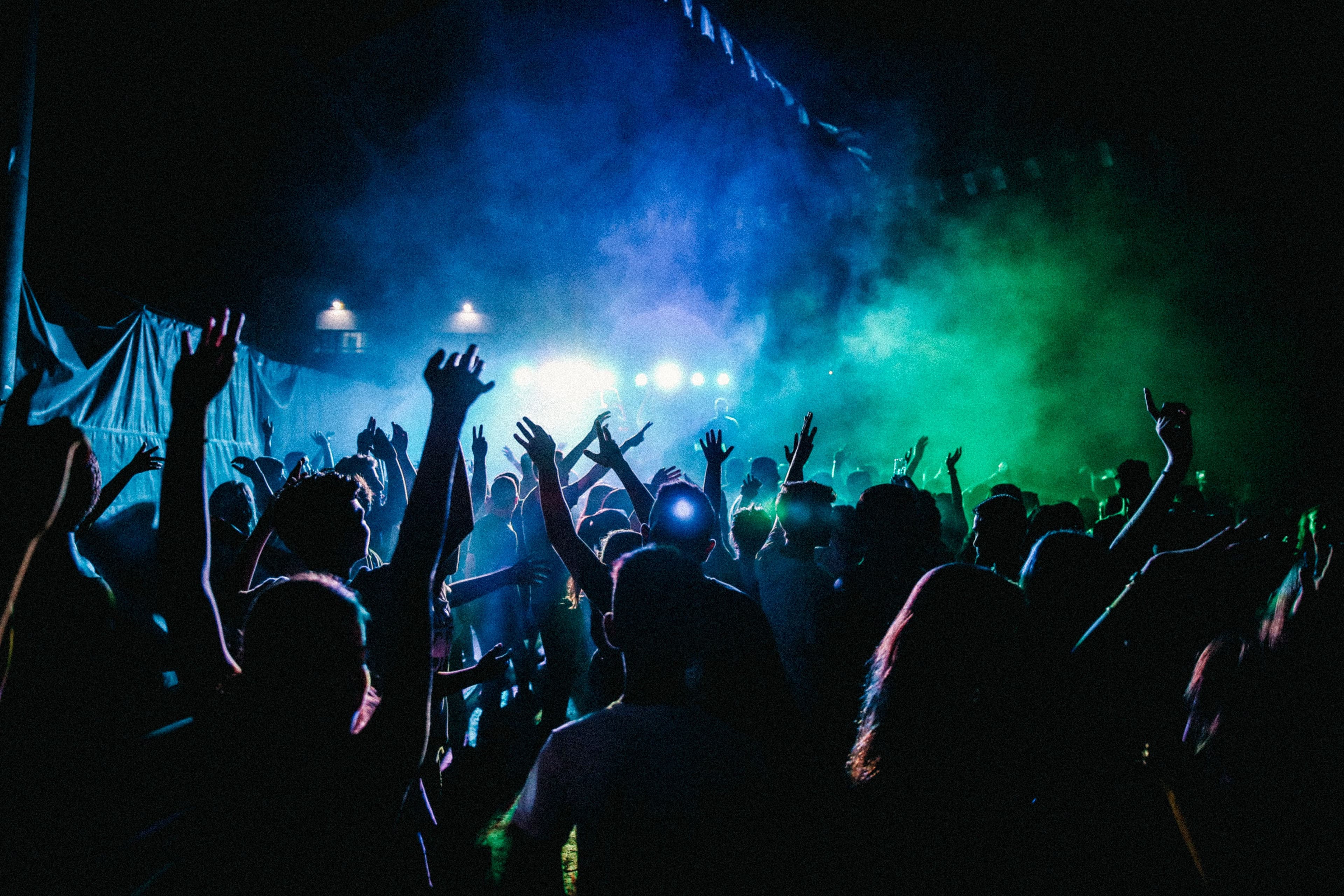 Crowd with hands raised under blue and green stage lights